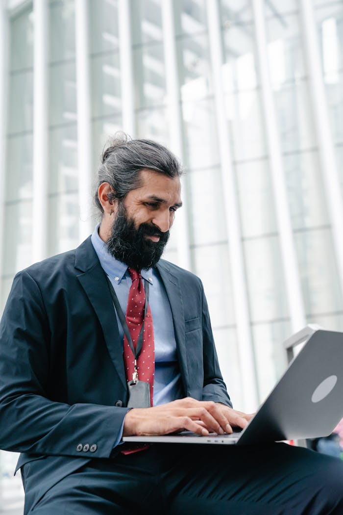 Bearded professional man in formal wear working on a laptop indoors.